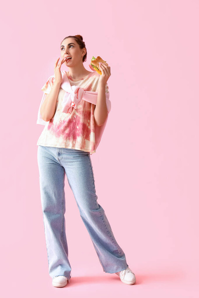 Mujer joven con sabroso sándwich sobre fondo rosa
 - Foto, Imagen