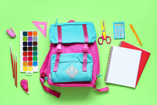 Elegante mochila escolar y diferentes artículos de papelería sobre fondo verde - Foto, Imagen