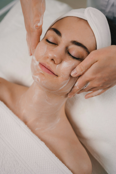 Vista de perto de uma bela mulher deitada na cama enquanto faz o tratamento de limpeza do rosto com espuma. Tratamento de massagem corporal. Tratamento terapêutico, pele de beleza - Foto, Imagem