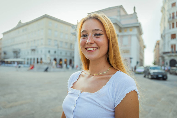Портрет привлекательной улыбчивой рыжей девушки в центре города летом - Фото, изображение