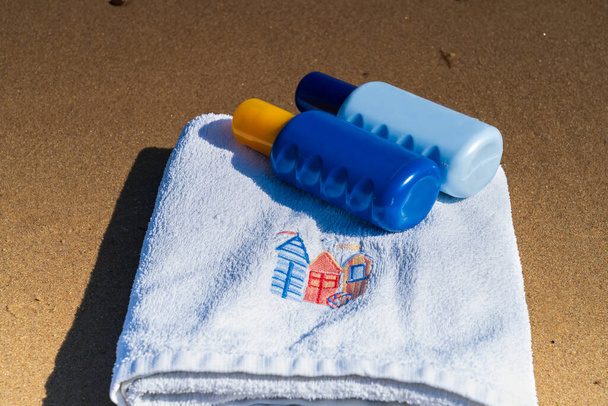 Strand törölköző és napbarnító spray palackok a strandon. Nyaralás / nyaralás koncepció - Fotó, kép