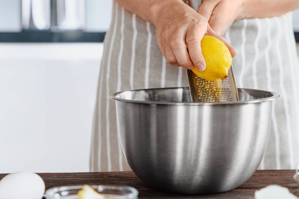 Die Hände des Kochs reiben die Schale einer Zitrone in eine Teigschüssel. Natürliches Aroma in vidi Zitronenschale. Zubereitung von Zutaten in Bäckerei- oder Restaurantküche - Foto, Bild