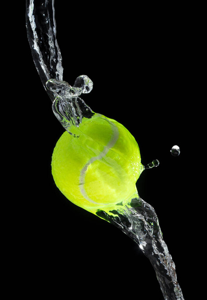 balle de tennis a frappé l'eau et éclabousser dans l'air. Boule de tennis verte voler sous la pluie et éclabousser spin éclaboussure dans l'eau gouttelette. fond noir isolé gel action - Photo, image
