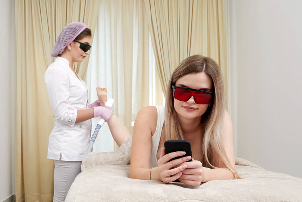 Skupiając się na nowoczesnych trendach urody, spokojna kobieta doświadcza precyzji technik laserowych włosów na nogach w dobrze wyposażonym salonie - Zdjęcie, obraz