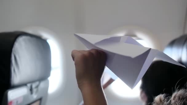 Vista trasera, los niños en el avión se ve soñadoramente por la ventana y juega con el avión de papel. Niño sueña con trabajar como piloto mientras mira al cielo y juega con el juguete de papel del avión.  - Imágenes, Vídeo