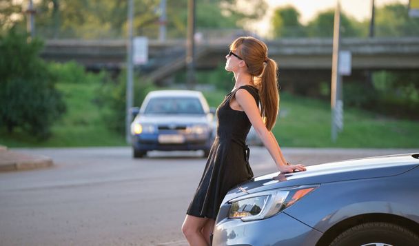 Счастливая женщина-водитель в повседневной одежде наслаждается теплым днем рядом со своей машиной на летней улице. Концепция путешествий и транспорта. - Фото, изображение