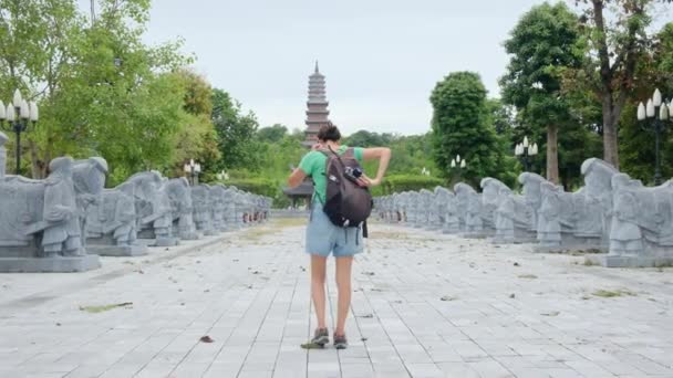 40-jarige vrouw met rugzak wandelen door Zuidoost-Aziatische tempel, het vastleggen van cultuur en empowerment  - Video