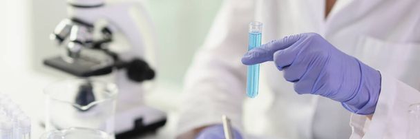 Крупним планом жінка-хімік дивиться на пробірку з блакитною рідиною перед мікроскопом. Контроль якості концепції миючих засобів
 - Фото, зображення
