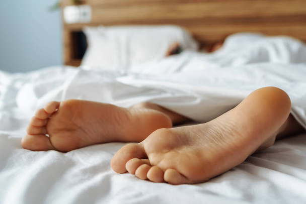 pés nus menina deitada na cama espreitar debaixo de coberturas - Foto, Imagem