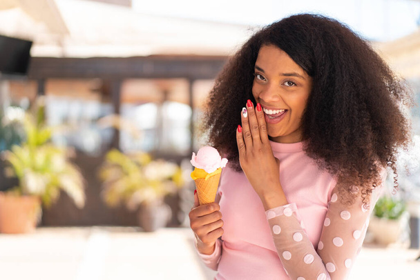 Joven mujer afroamericana con un helado de corneta al aire libre susurrando algo - Foto, imagen