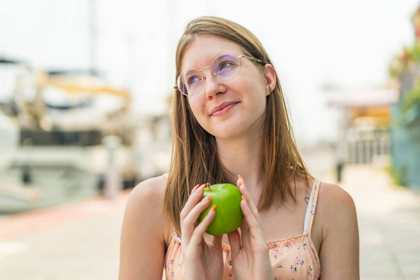 Νεαρή Γαλλίδα με γυαλιά σε εξωτερικούς χώρους κρατώντας ένα μήλο - Φωτογραφία, εικόνα