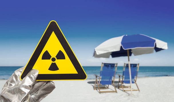 sinal de aviso de radiação nuclear em frente a espreguiçadeiras e oceanos turvos - Foto, Imagem