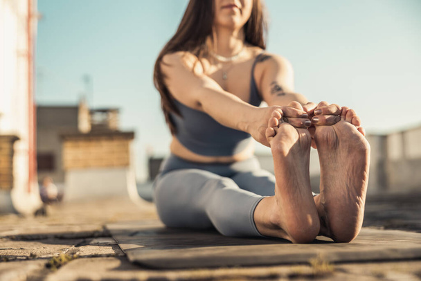 Close-up of a woman practicing yoga stretching exercise on a rooftop terrace. - 写真・画像