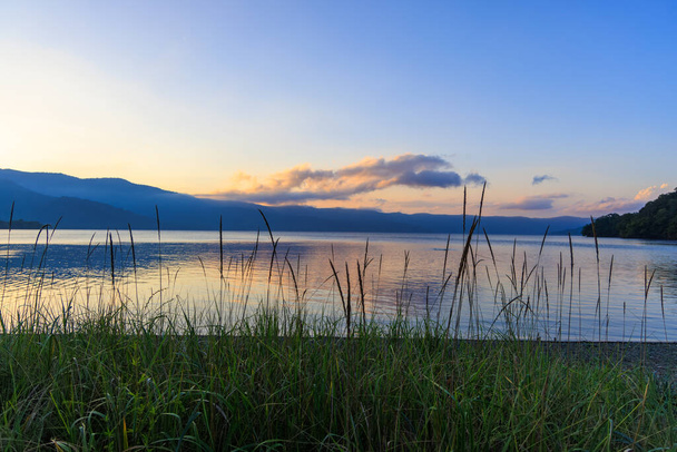 Green grass by shore of Lake Kussharo in Hokkaido, Japan at sunset. High quality photo - Photo, Image