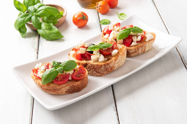 Поднос вкусной капрезе брускетте, типичные итальянские закуски с моцареллой, помидорами, базиликом, черными оливками, ореганом и оливковым маслом - Фото, изображение