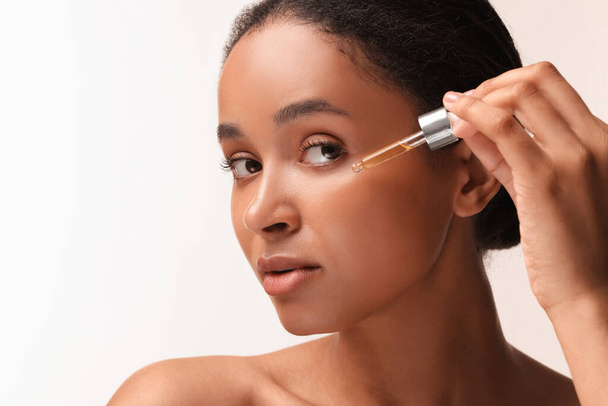 Beautiful woman applying serum onto her face on white background, closeup. Space for text - Foto, afbeelding