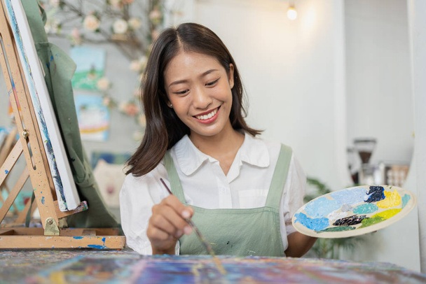 Aasialainen nainen maalaa taidetta. Hän on ammattitaiteilija. Vesiväritaiteilija maalaa taidetta paperille. Freelance-taiteilija maalaa akvarellilla. Luova taideteos akvarellilla. Taide piirustus ideoita. - Valokuva, kuva