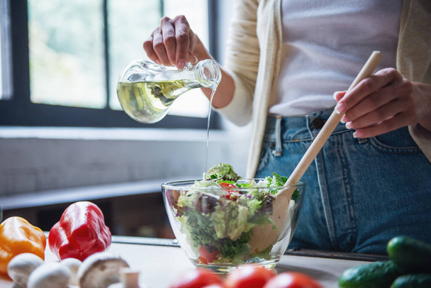 Cropped image of beautiful young girl mixing salad while cooking in kitchen at home - Photo, Image