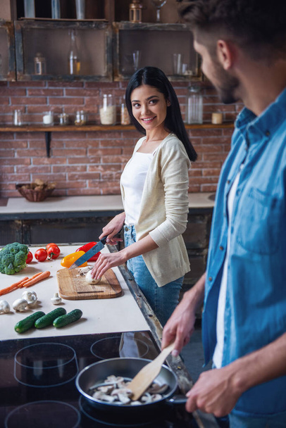 Bella giovane coppia sta parlando e sorridendo mentre cucina in cucina a casa
 - Foto, immagini