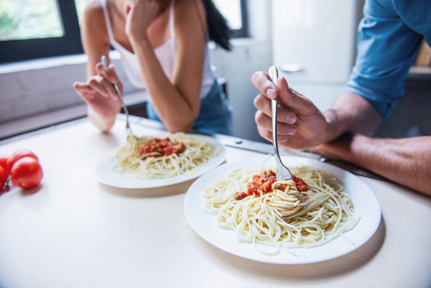 abgeschnittenes Bild eines schönen jungen Paares, das Spaghetti in der heimischen Küche isst - Foto, Bild