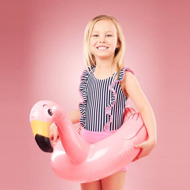 Dziecko dziewczyna, lato i strój kąpielowy z nadmuchiwane, flamingo i szczęście z wakacji na różowym tle. Stroje kąpielowe, zabawy i zabawki dla zwierząt, szczęśliwy dzieciak w portrecie i zabawy z wakacjami w studio. - Zdjęcie, obraz