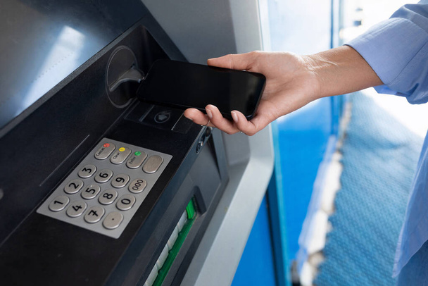 zbliżenie kobieta przyniósł smartfon dla bezdotykowe korzystanie z w ATM. - Zdjęcie, obraz