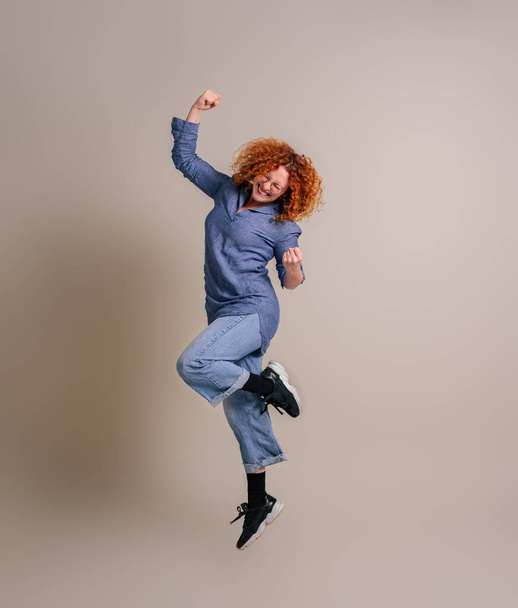 Возбужденная деловая женщина с рыжеволосой трясущей кулаком и экстатично прыгающая на заднем плане - Фото, изображение