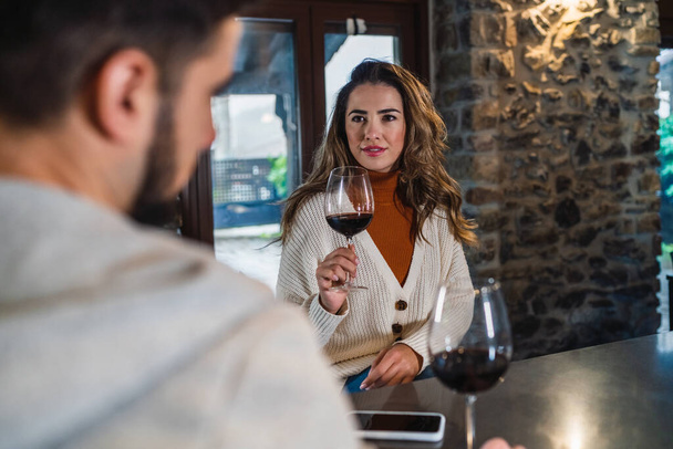 A young woman smiling with the couple with a glass of red wine on a romantic and happy evening in the kitchen of their home, lifestyle of a couple. - Photo, Image