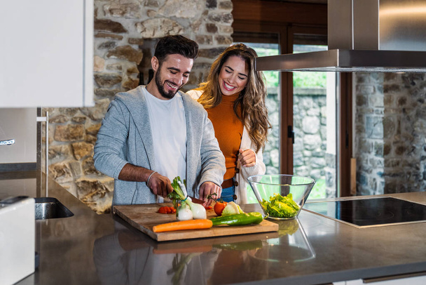 Ein junger Mann bereitet in der Küche seines Landhauses einen Salat für seine Freundin zu, Lebensstil eines glücklichen Paares. - Foto, Bild