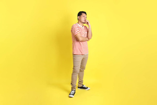 Der erwachsene asiatische Mann in lässiger Kleidung steht auf gelbem Hintergrund. - Foto, Bild
