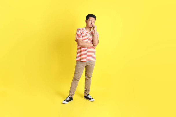 El hombre asiático adulto en ropa casual de pie sobre el fondo amarillo. - Foto, imagen
