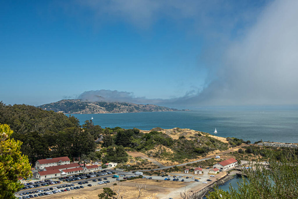 San Francisco, CA, USA - 12 Ιουλίου 2023: Σταθμός Ακτοφυλακής των ΗΠΑ Golden Gate στο Horseshoe κόλπο και μικρότερο σπίτι Presidio Yacht Club κάτω από ομίχλη πάνω από μεγαλύτερο κόλπο του Σαν Φρανσίσκο - Φωτογραφία, εικόνα