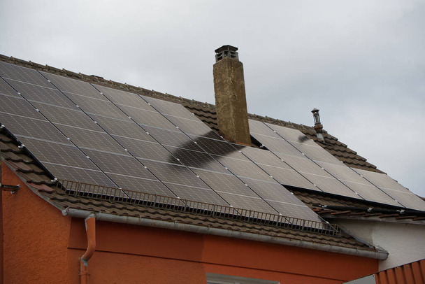 Solar panels on a residential building roof. The sky is gray most of the time, but some sun shines on the panels and electricity is being produced - Photo, Image
