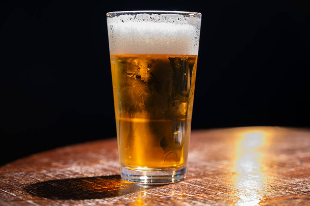 Pintová sklenice studeného čerstvého britského piva a ležáckého piva podávaná ve staré staroanglické hospodě, tmavé pozadí - Fotografie, Obrázek
