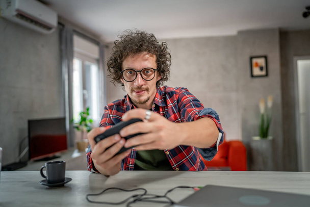 Кавказский мужчина сидит дома и играет в видеоигры на смартфоне - Фото, изображение