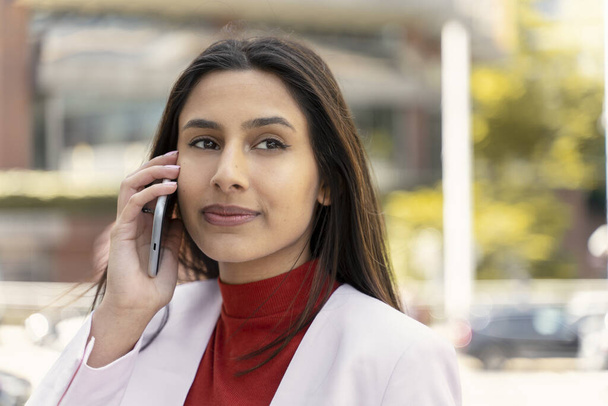 Kendine güvenen güzel bir Hintli kadının cep telefonuyla konuşan, telefona cevap veren şehir sokağına bakan güzel bir portresi. Teknoloji konsepti  - Fotoğraf, Görsel