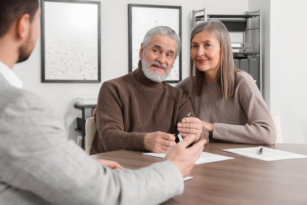 Elderly couple consulting insurance agent about pension plan at wooden table indoors - Foto, imagen