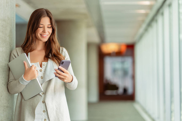 Portrait of beautiful smiling woman, worker holding mobile phone, laptop working online, check email in modern office. Successful happy freelancer receive payment. Technology, mobile banking concept - Photo, Image