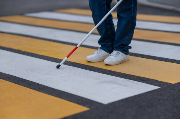 Close-up of the legs of a blind woman crossing the road at a crosswalk with a cane - Foto, Bild