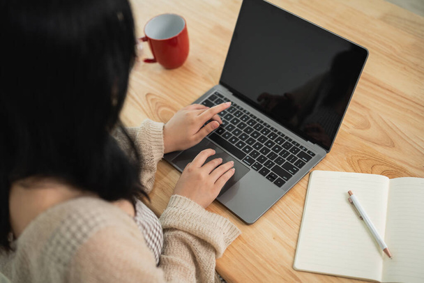 Азіатська позаштатна жінка носить окуляри на клавіатурі і працює на ноутбуці на дерев'яному столі вдома. Жінка-підприємець, яка працює для свого бізнесу у вітальні. Концепція домашньої роботи бізнесу. - Фото, зображення