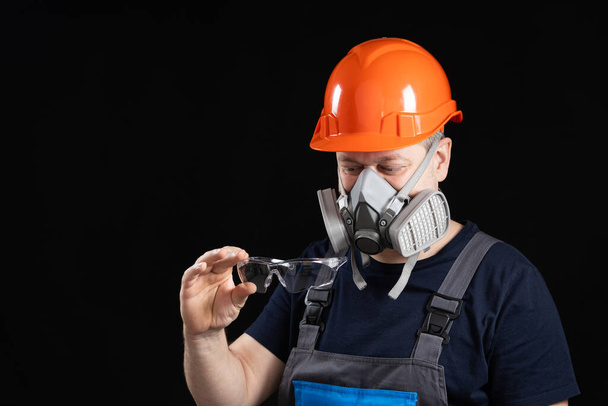 Ein Mann mit Helm, Atemschutzmaske und Schutzbrille auf schwarzem Hintergrund. - Foto, Bild