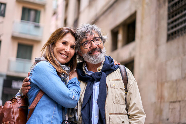 Kaukasisches lächelndes älteres Touristenliebhaberpaar, das sich im Freien umarmt. Glückliche erwachsene Menschen umarmten sich romantisch. Mann und Frau schauen sich etwas liebevoll genussvolles Wochenende an. - Foto, Bild