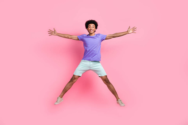 Full size photo of good mood guy wear blue t-shirt white stylish pants flying jumping in star pose isolated on pink color background. - Fotoğraf, Görsel