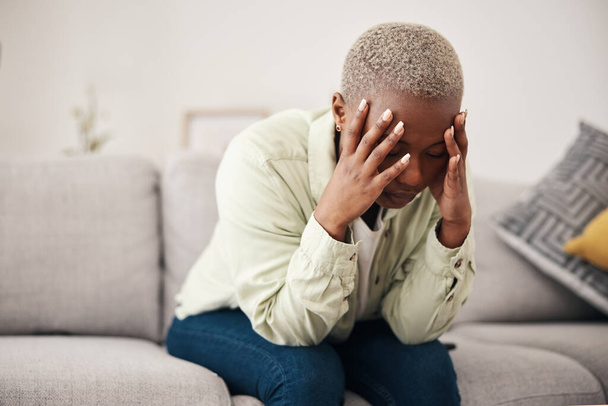 Stress, hoofdpijn en duizeligheid met een zwarte vrouw op een bank in de woonkamer van haar huis voor geestelijke gezondheid. Angst, burn-out of pijn en een jongere in een appartement met depressie of migraine. - Foto, afbeelding