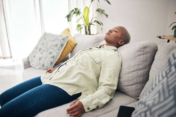 Müde, schlafende und schwarze Frau auf dem heimischen Sofa zum Entspannen, Stressabbau oder faul nach der Arbeit. Psychische Gesundheit, Wohnzimmer und ein afrikanisches Mädchen auf einer Couch zum Ausruhen, Schlafen oder Burnout mit Schlaflosigkeit oder Erschöpfung. - Foto, Bild
