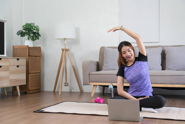 Jovem mulher asiática assistindo vídeo fitness no laptop para treinar e fazer exercício para esticar o braço. - Foto, Imagem