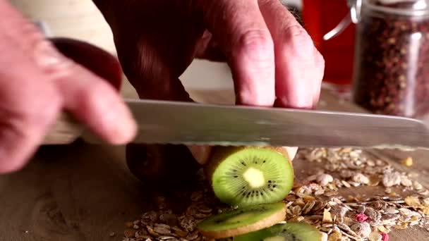A chef slices kiwis in a kitchen with a knife on a wooden board.  - Footage, Video
