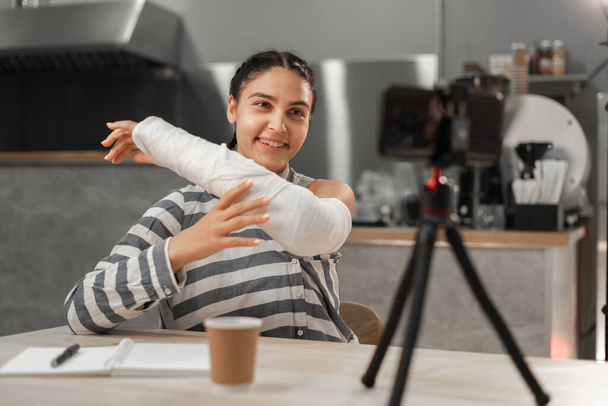 Ευτυχισμένο κορίτσι δείχνει σπασμένο χέρι χρησιμοποιώντας το smartphone app απολαμβάνοντας online εικονική συνομιλία βιντεοκλήση με φίλους σε εικονική συνάντηση, γράφοντας στο σημειωματάριο. Αντιγραφή χώρου - Φωτογραφία, εικόνα