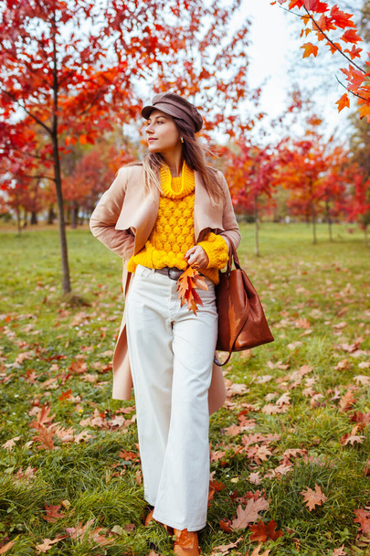Full body portrait of beautiful woman wearing stylish warm clothes in autumn park among red trees. Female fall fashionable outfit. Modern accessories - Photo, Image