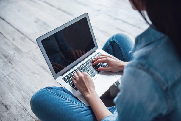 Imagen recortada de la hermosa chica en ropa de jean usando un ordenador portátil mientras está sentado en el suelo
 - Foto, Imagen